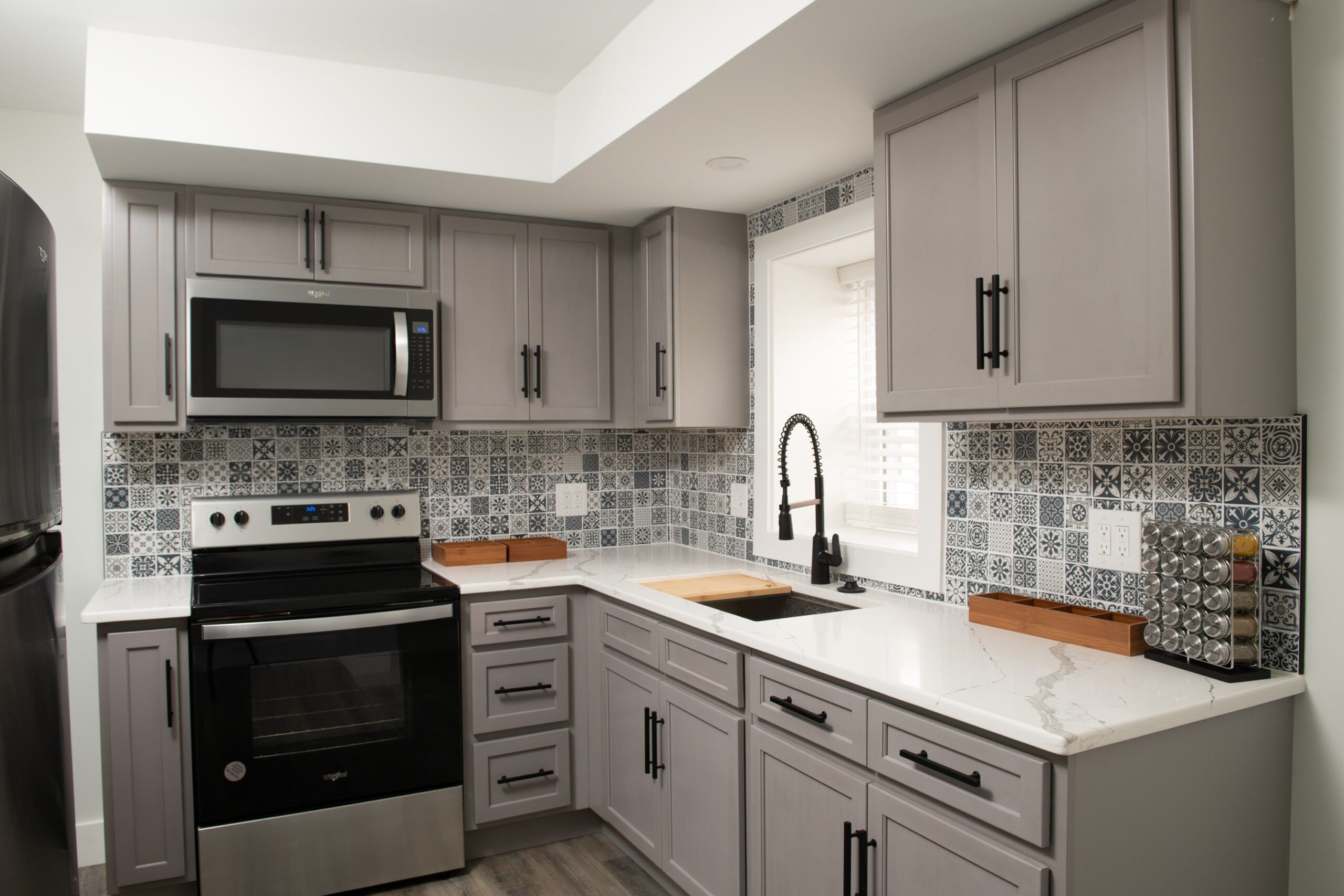 An image of a kitchen with gray cabinets with a gray mosaic backsplash.