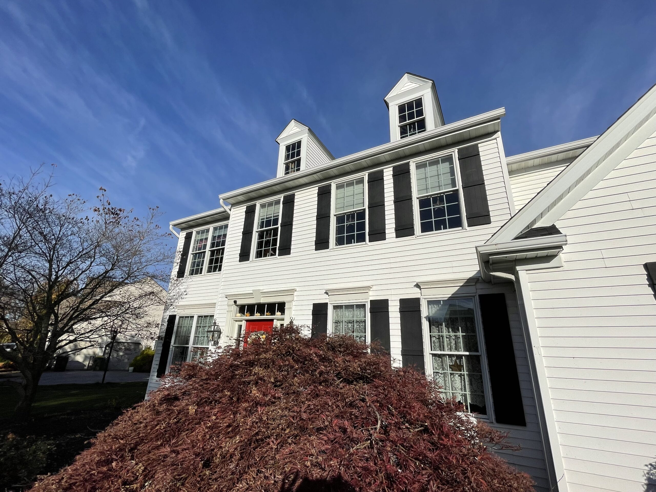 An image of the front of a home with white siding and a small tree in front.