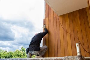 A worker installing wood siding on a building.