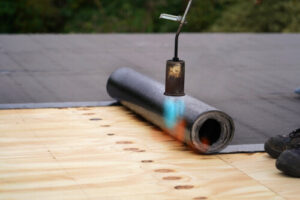 torching a roll of black flat roofing membrane