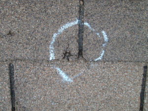 a divot in shingle is outlined in chalk to show hail damage