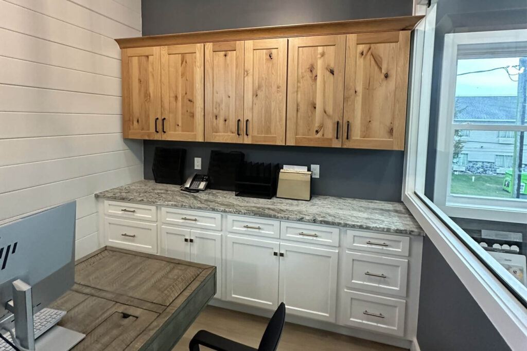 A commercial office renovation example with wooden cabinets above a marble countertop next to a desk with a computer