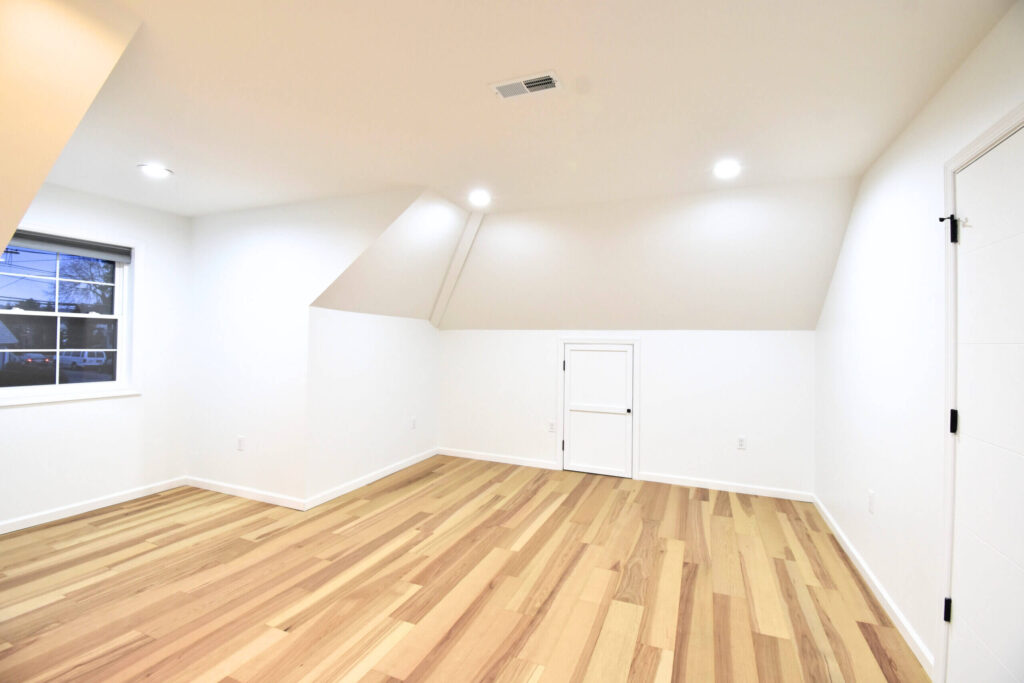 The inside of a completed affordable home addition of a bedroom with a closet. The walls are white and the floors are hardwood.