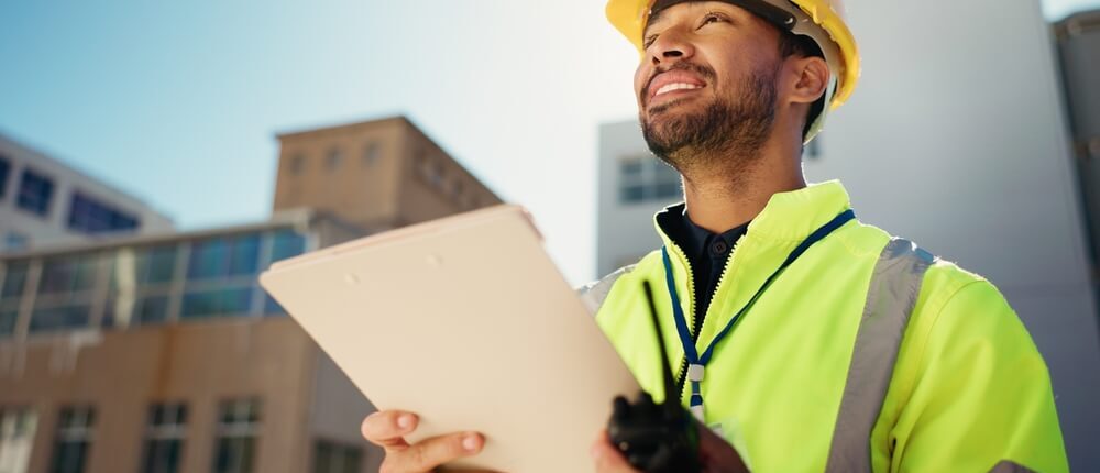 Contractor in a hard hat and neon vest holds a folder in his hands as he handles the residential building permits for a build
