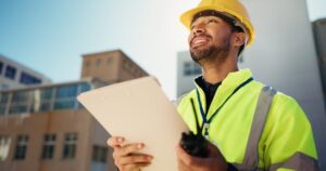Contractor in a hard hat and neon vest holds a folder in his hands as he handles the residential building permits for a build