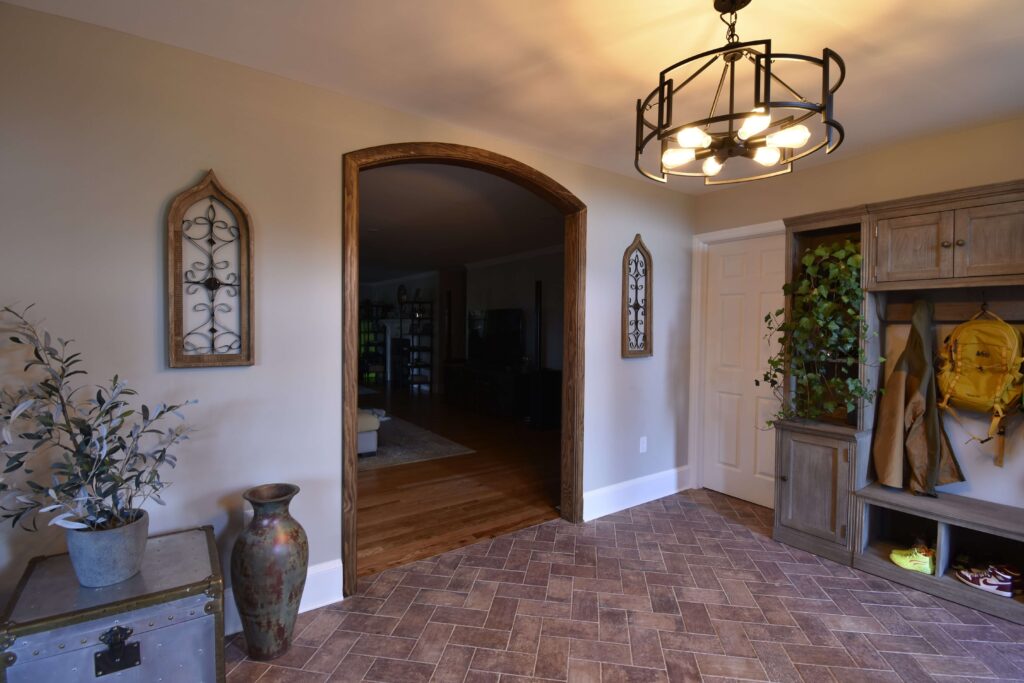 Finished residential front room home remodel at an angle with wood trim around an archway and a wooden coat rack against one wall. An industrial light fixture hangs from the ceiling
