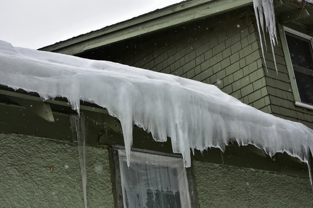 Ice dam at the edge of a residential roof, with icicles hanging down.