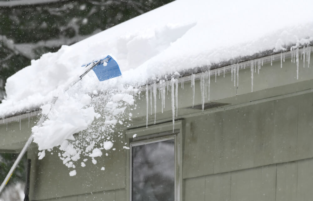 Someone using a rake to remove snow from their roof