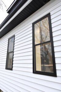 Exterior of a house with white siding and two windows with black trim